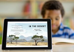 Student out of focus in background behind tablet in focus, with In the Desert book jacket displayed on device.